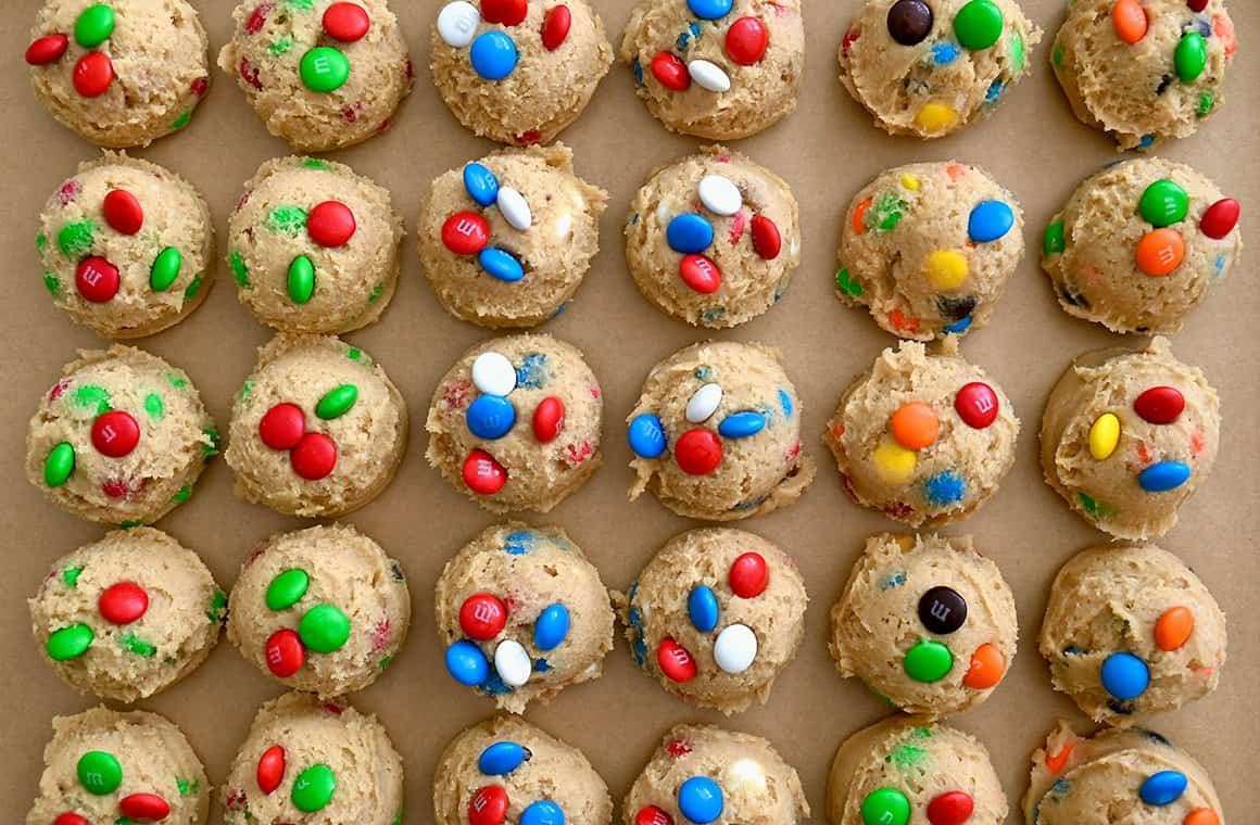 A top-down view of scooped dough studded with candy-coated chocolates  