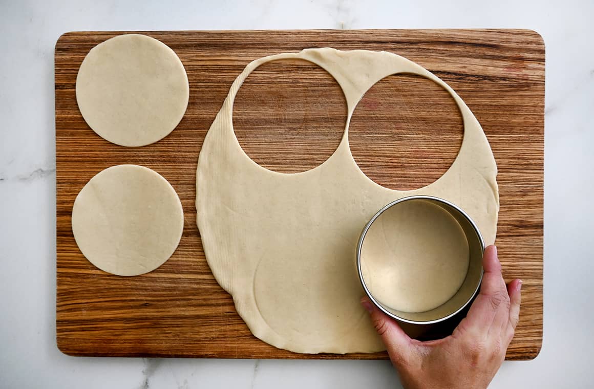 A hand holding a round cookie cutter stamps out round dough circles