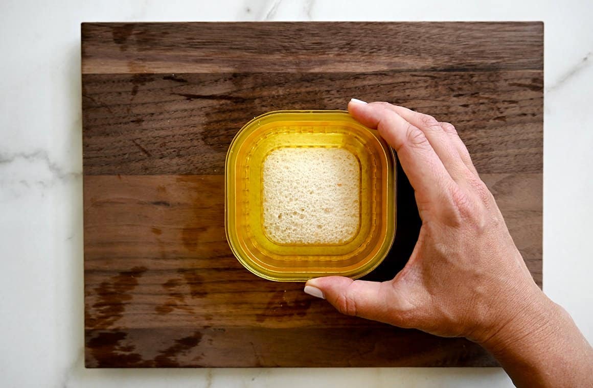 A wood cutting board with a homemade Uncrustables peanut butter and jelly sandwich