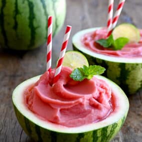 Watermelon Slushies in a half hollowed-out watermelon with a straw and a lime wedge garnish