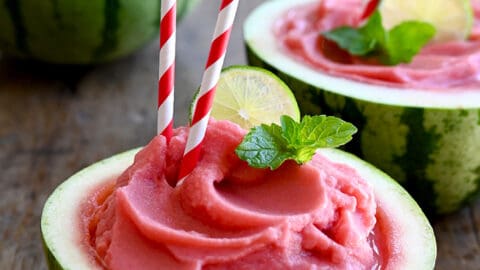 Watermelon Slushies in a half hollowed-out watermelon with a straw and a lime wedge garnish