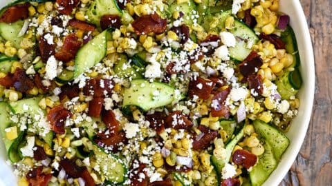 A top-down view of Corn and Zucchini Salad with Basil Vinaigrette in a large white serving bowl next to a small bowl filled with cotija cheese