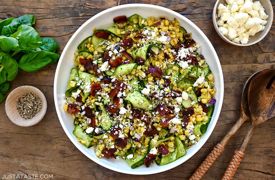 A white serving bowl containing the best fresh corn and zucchini salad tossed in a basil vinaigrette and topped with cotija cheese