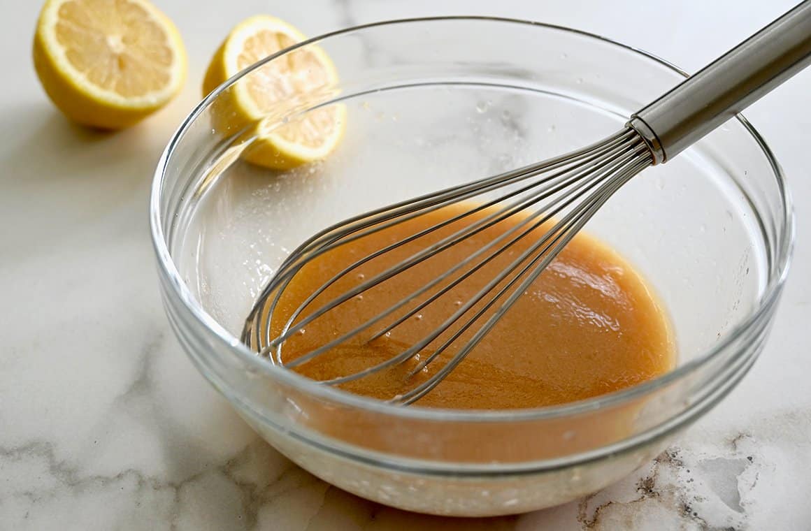 A whisk rests in a clear bowl that contains a homemade vinaigrette