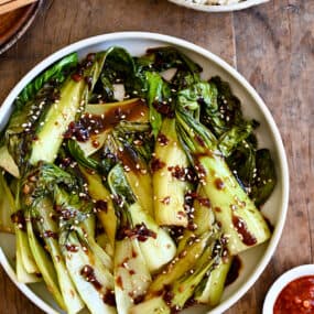 A white bowl with bok choy drizzled with soy sauce