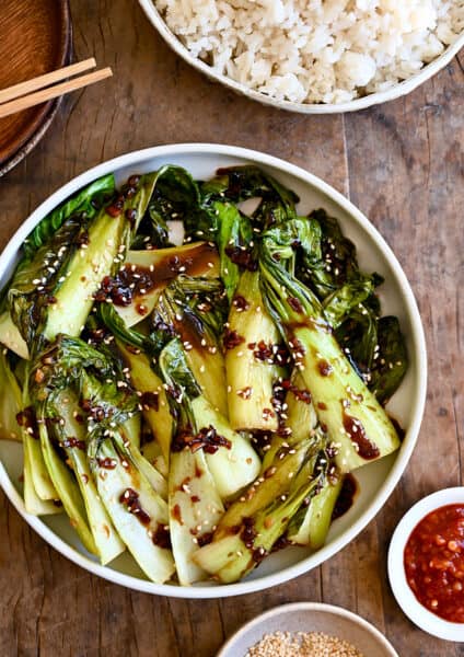 A white bowl with bok choy drizzled with soy sauce
