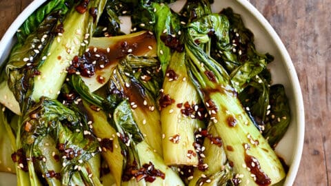 A white bowl with bok choy drizzled with soy sauce