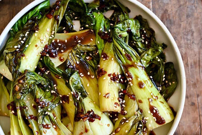 A white bowl with bok choy drizzled with soy sauce