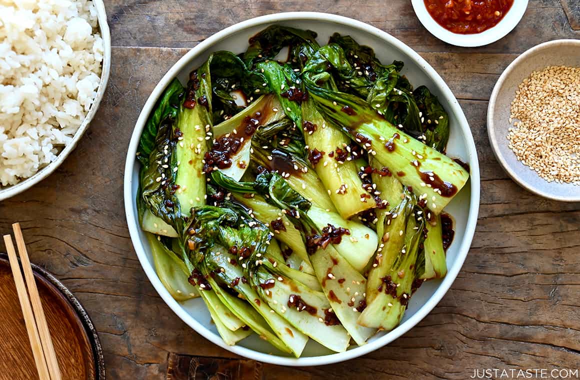 A top-down view of a white bowl containing bok choy next to a bowl of white rice