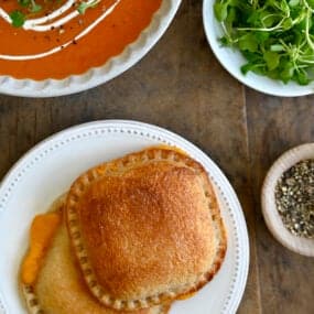 A top down view of two grilled cheese sandwiches next to a bowl of tomato soup