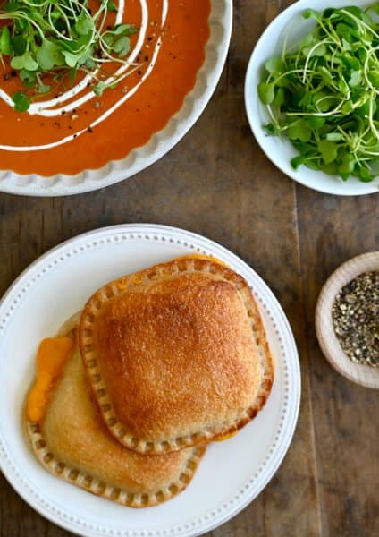 A top down view of two grilled cheese sandwiches next to a bowl of tomato soup