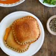 A top-down view of two Air Fryer Grilled Cheese sandwiches on a plate next to a bowl of tomato soup and a plate topped with micro greens.