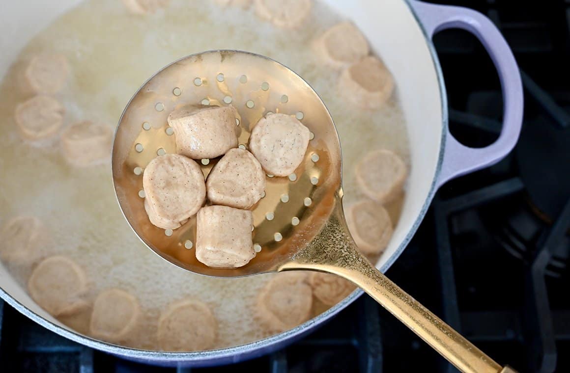 A slotted spoon with dough pieces over a large pot containing water and baking soda