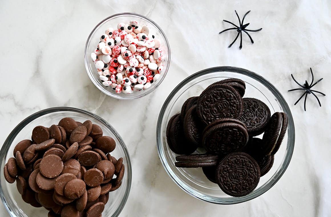 A top-down view of clear bowls containing Oreo cookies, chocolate melting wafers and bloodshot candy eyes