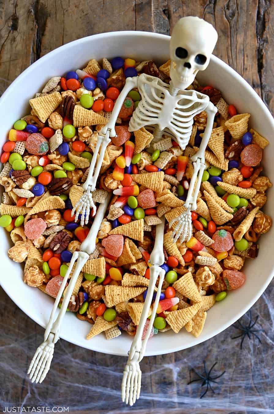 A top-down view of a white serving bowl containing Halloween Snack Mix and a plastic skeleton