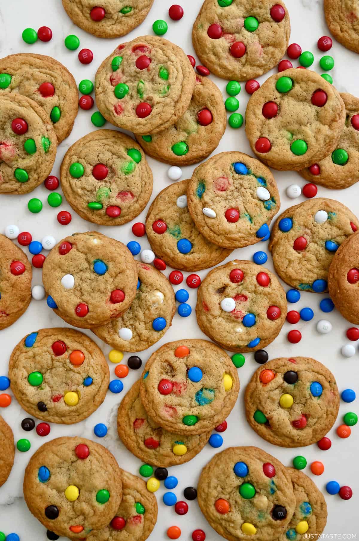 An assortment of bakery-style M&M cookies with M&M candies scattered around the cookies.