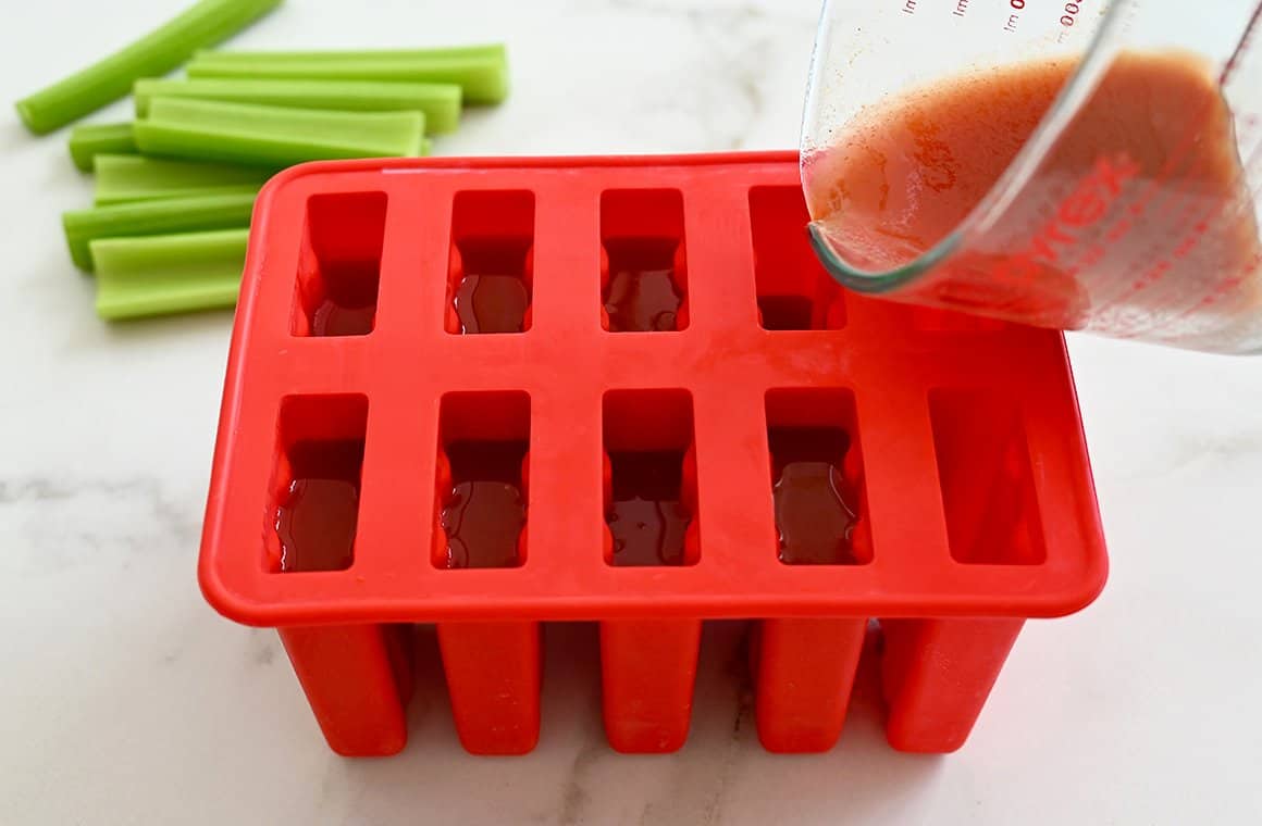 Bloody Mary mix being poured into silicone popsicle molds from a liquid measuring cup