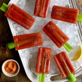 A top-down view of Bloody Mary Popsicles with celery sticks over ice