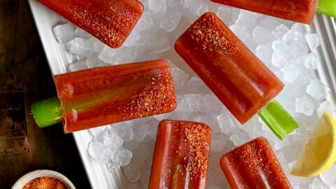 A top-down view of Bloody Mary Popsicles with celery sticks over ice