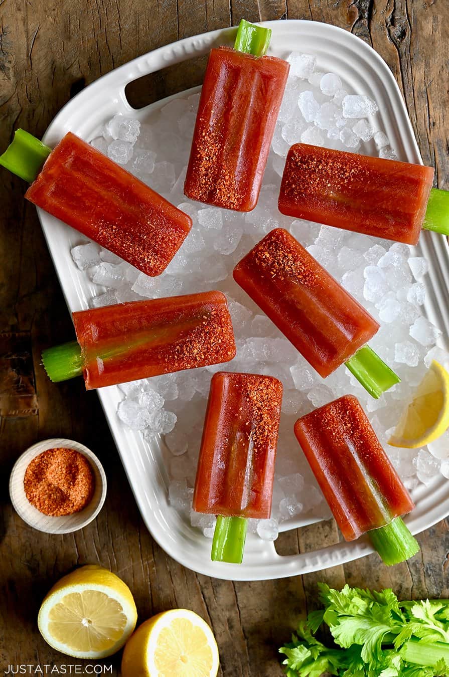 A top-down view of Bloody Mary Popsicles with celery sticks and Tajin seasoning over ice