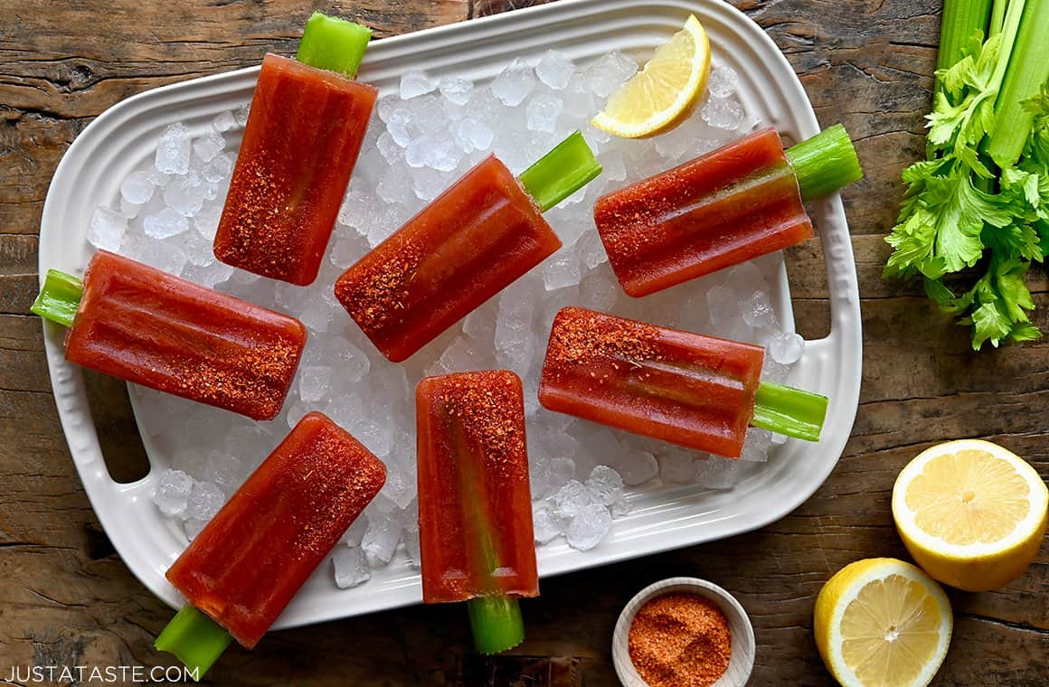 A top-down view of Bloody Mary Popsicles garnished with Tajin seasoning over a tray with ice