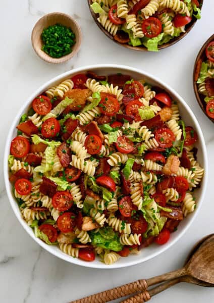 BLT pasta salad in a large serving bowl next to wood serving spoons.