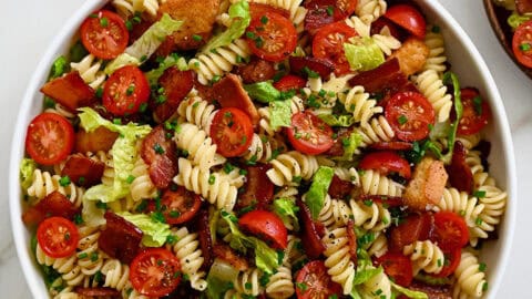 BLT pasta salad in a large serving bowl next to wood serving spoons.