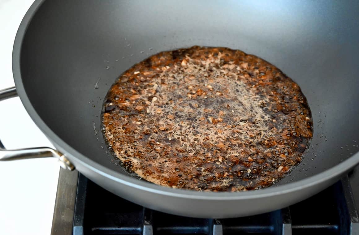 A wok on the stovetop containing soy sauce, garlic and brown sugar