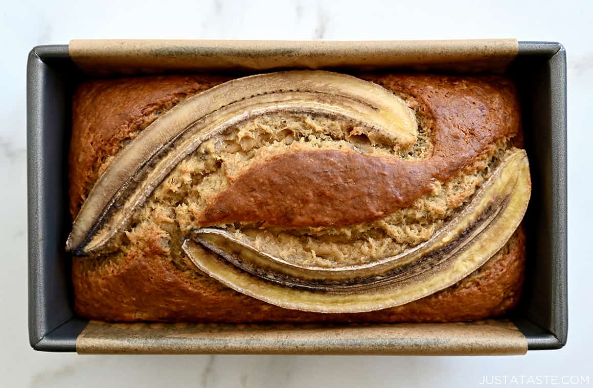 A top-down view of a loaf pan containing perfectly golden brown butter banana bread topped with banana slices
