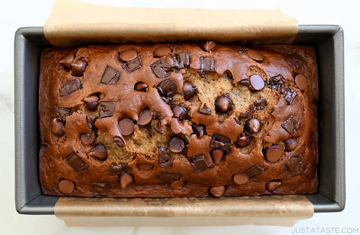 A top-down view of extra-moist Buttermilk Banana Bread studded with chocolate chips and chunks in a parchment paper-lined loaf pan