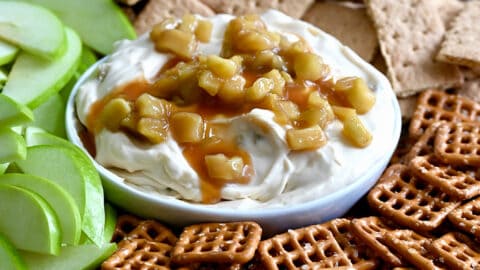 Caramel Apple Cheesecake Dip in a bowl on a plate surrounded by pretzels, green apple slices, and graham crackers