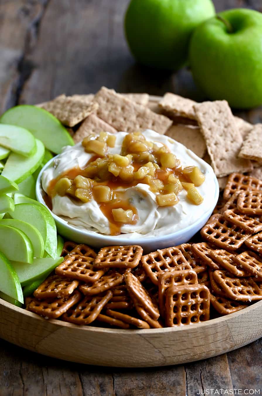 Caramel Apple Cheesecake Dip in a bowl on a plate surrounded by pretzels, green apple slices, and graham crackers