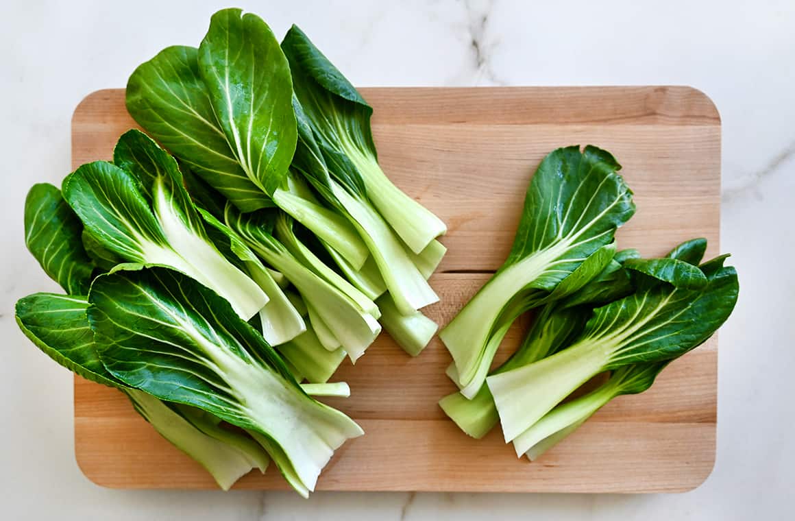 A wood cutting board containing bok choy leaves