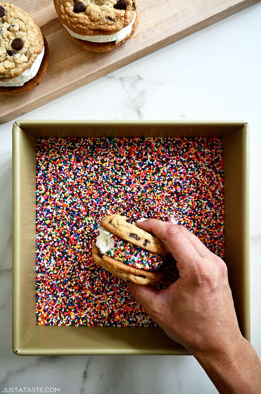 A cookie ice cream sandwich being rolled in rainbow sprinkles