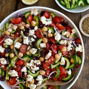 A large serving bowl containing Greek cucumber tomato salad with crumbled feta cheese