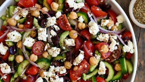 A large serving bowl containing Greek cucumber tomato salad with crumbled feta cheese