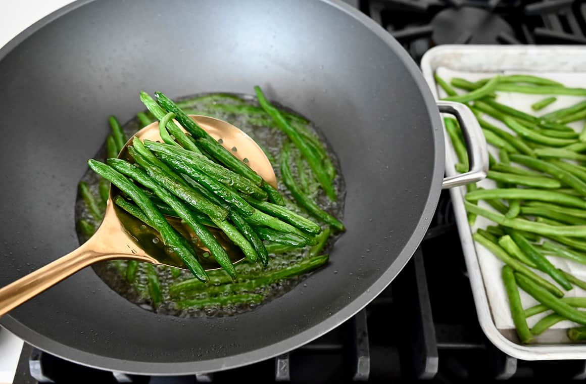 Fried green beans in a slotted spoon held over a wok