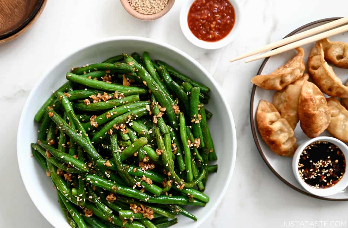 Garlic Chinese Green Beans in a white bowl next to a plate with fried dumplings
