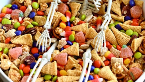 A white bowl containing easy Halloween Snack Mix and a small plastic skeleton