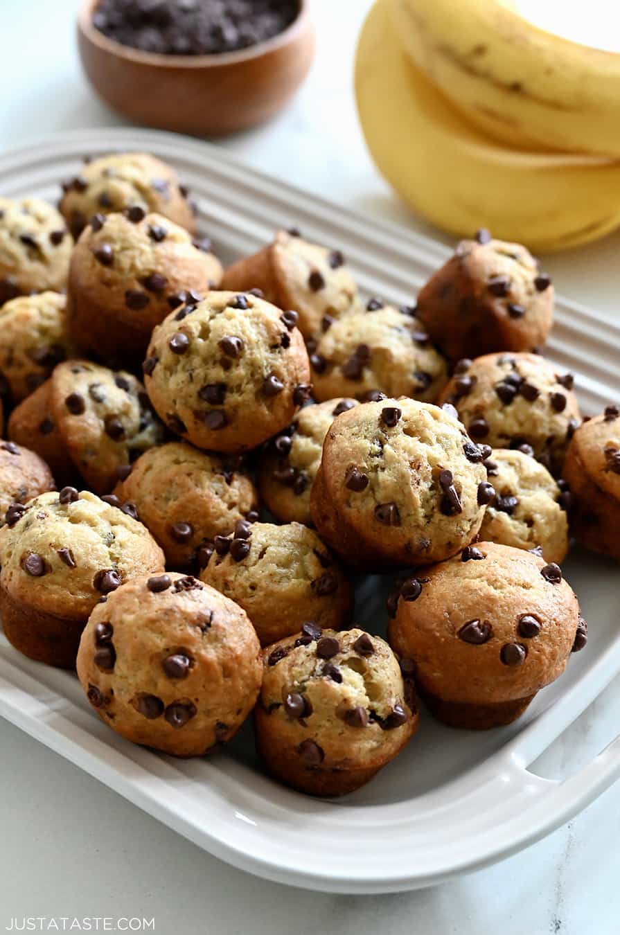 Mini Chocolate Chip Banana Muffins on a white serving platter next to a bunch of ripe bananas