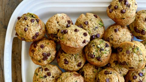 A top-down view of Mini Zucchini Muffins piled high on a white serving platter