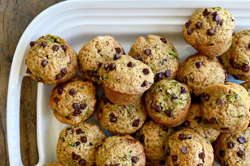 A top-down view of Mini Zucchini Muffins piled high on a white serving platter