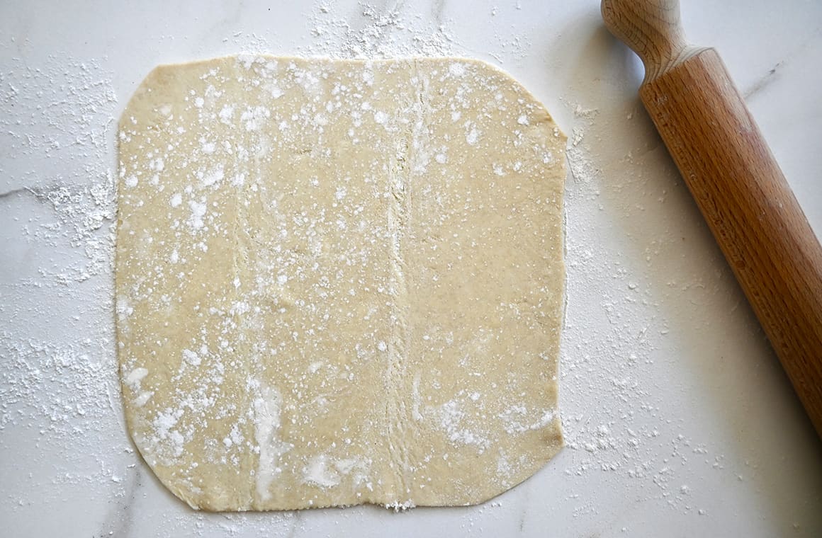 A top-down view of a puff pastry sheet on a lightly floured surface next to a rolling pin
