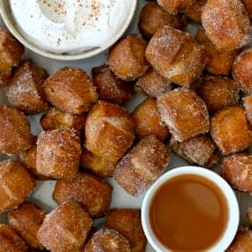 A top-down view of Pumpkin Spice Pretzel Bites surrounding a small bowl containing whipped cream and a small bowl containing caramel sauce