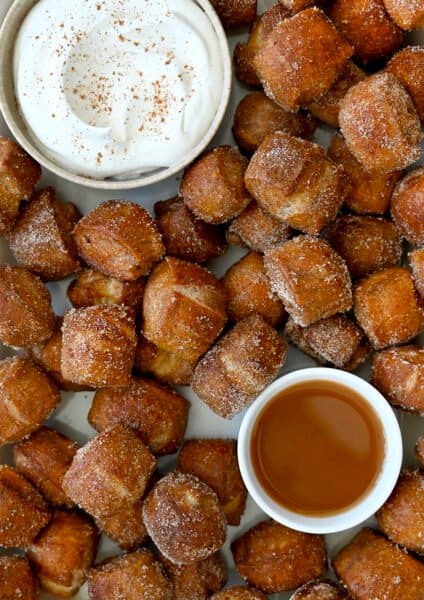 A top-down view of Pumpkin Spice Pretzel Bites surrounding a small bowl containing whipped cream and a small bowl containing caramel sauce