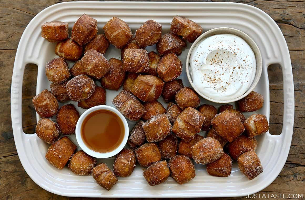 A top-down view of easy Pumpkin Spice Pretzel Bites on a white platter with small bowls containing whipped cream and caramel sauce