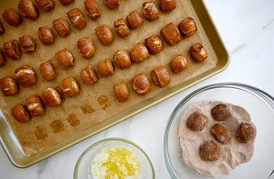 A top-down view of soft pretzels being tossed in a pumpkin spice and sugar mixture next to a baking sheet topped with soft pretzels