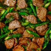 A close-up view of black pepper pork with asparagus pieces garnished with sesame seeds.