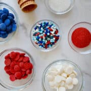 A top-down view of various sized bowls with red, white, and blue sprinkles and candy melts next to waffle cones.