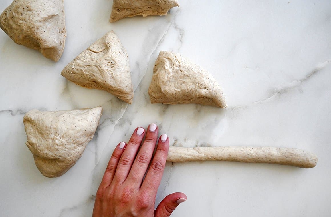 A hand rolls dough into a long log next to more dough pieces
